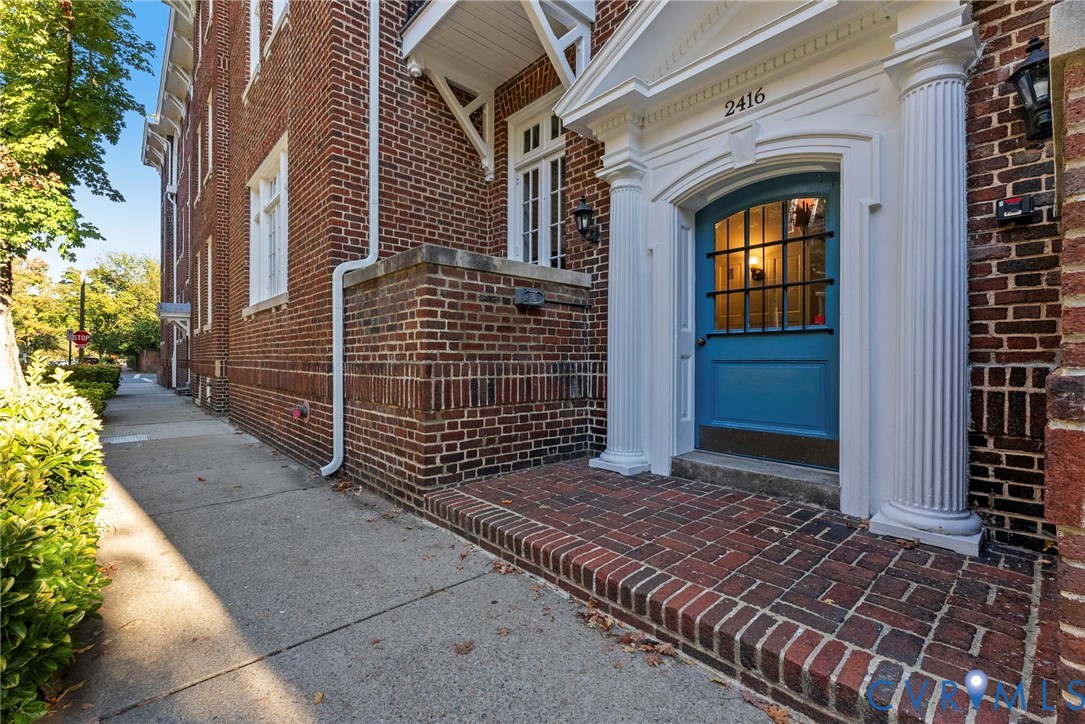 Brick exterior facade featuring a pedimented entryway with fluted columns, a blue-painted door with an iron grille window, and a brick porch