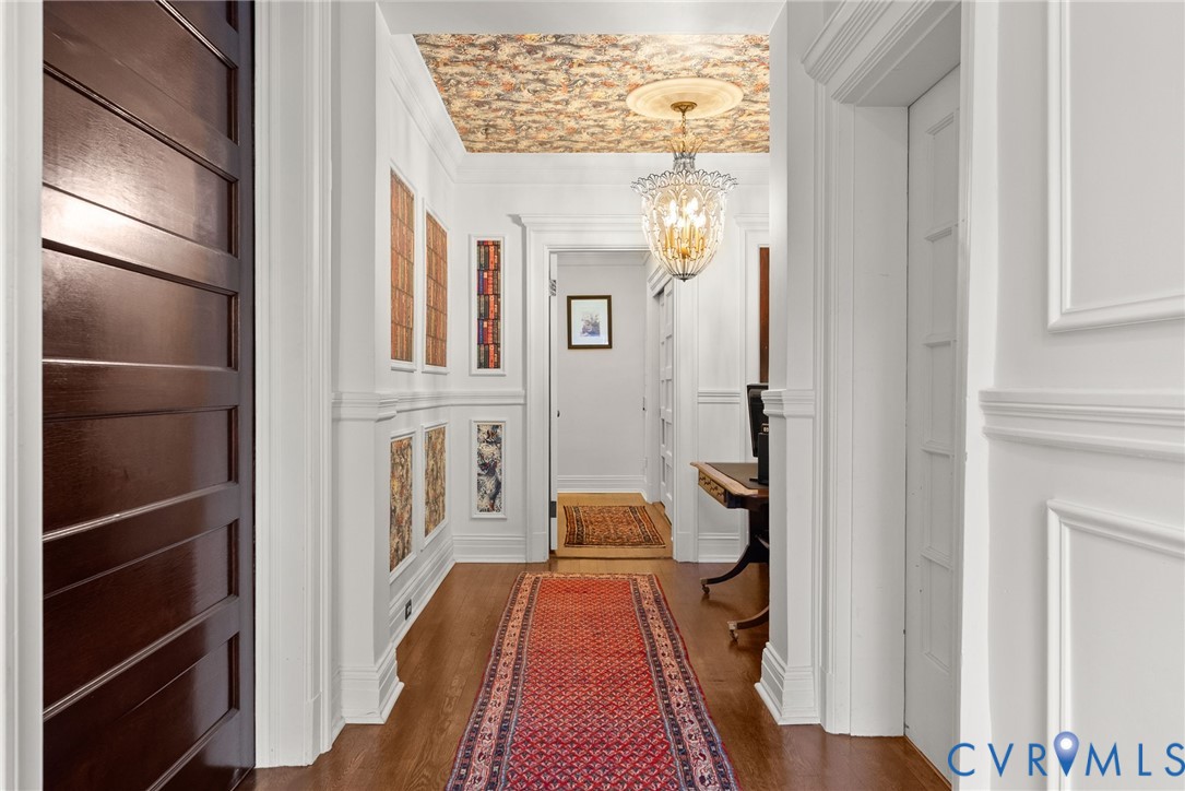 Entryway featuring wall wainscoting, a detailed ceiling medallion, a decorative hanging pendant light, custom wallpapered ceiling, and dark wood-finish flooring