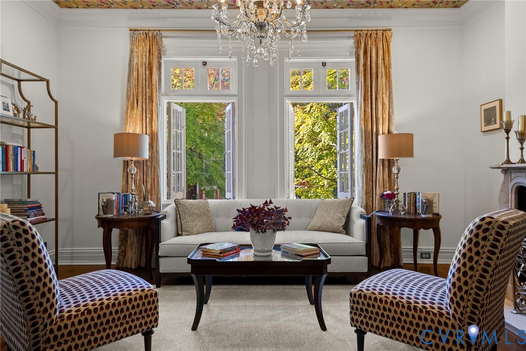 Living space featuring a crystal chandelier, intricate patterned ceiling detail, dual casement windows with arched transoms, and a classic fireplace mantel