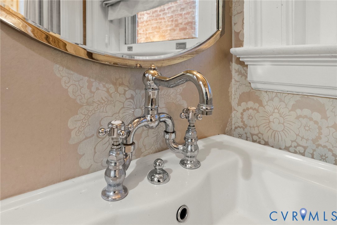 Polished chrome bridge-style faucet with cross-handle controls, white porcelain sink, and oval wall mirror with metallic frame