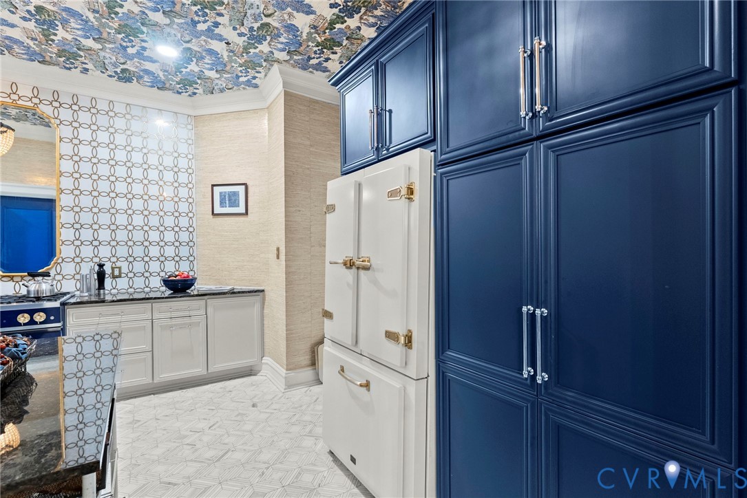 Custom navy blue cabinetry, integrated appliance featuring metallic latches, patterned tile backsplash, textured wall covering, and floral-motif ceiling finish