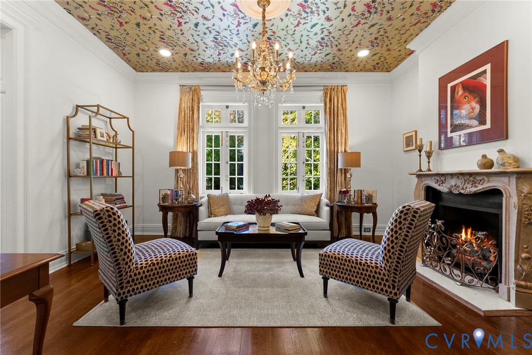Intricate patterned ceiling treatment, crystal chandelier, ornate carved fireplace surround, multi-pane windows, and wood-finish flooring