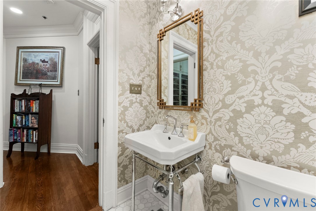 Powder room featuring patterned wallpaper, a wall-mounted brass-finish mirror, a white console sink with chrome legs, and hexagonal tile flooring