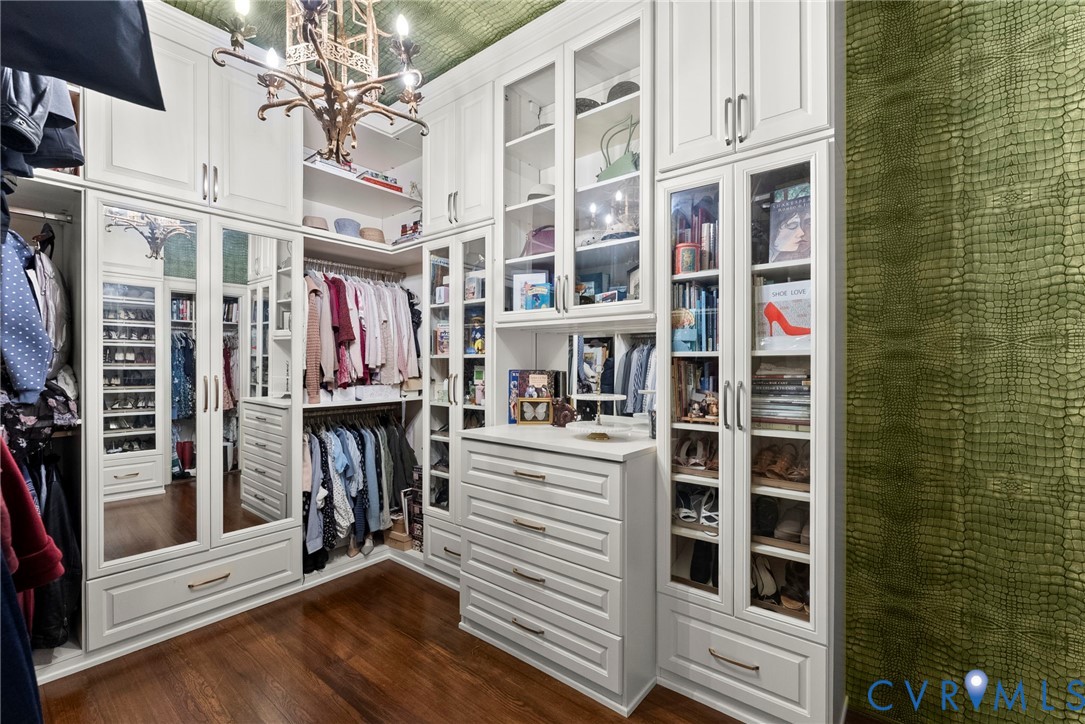 Custom floor-to-ceiling cabinetry with glass-front display doors, integrated drawer storage, mirrored door panels, wood-finish flooring, and ornate metal chandelier
