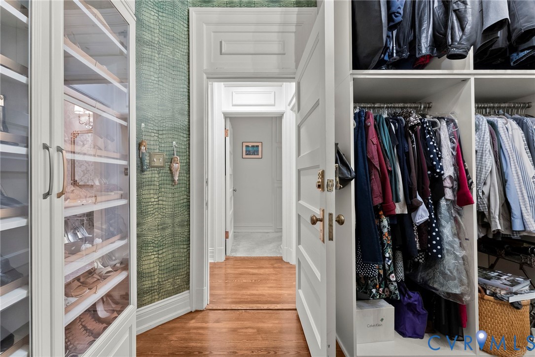 Custom built-in wardrobe cabinetry with glass-front shelving, textured green accent wall covering, multi-panel interior door with brass hardware, and hardwood flooring
