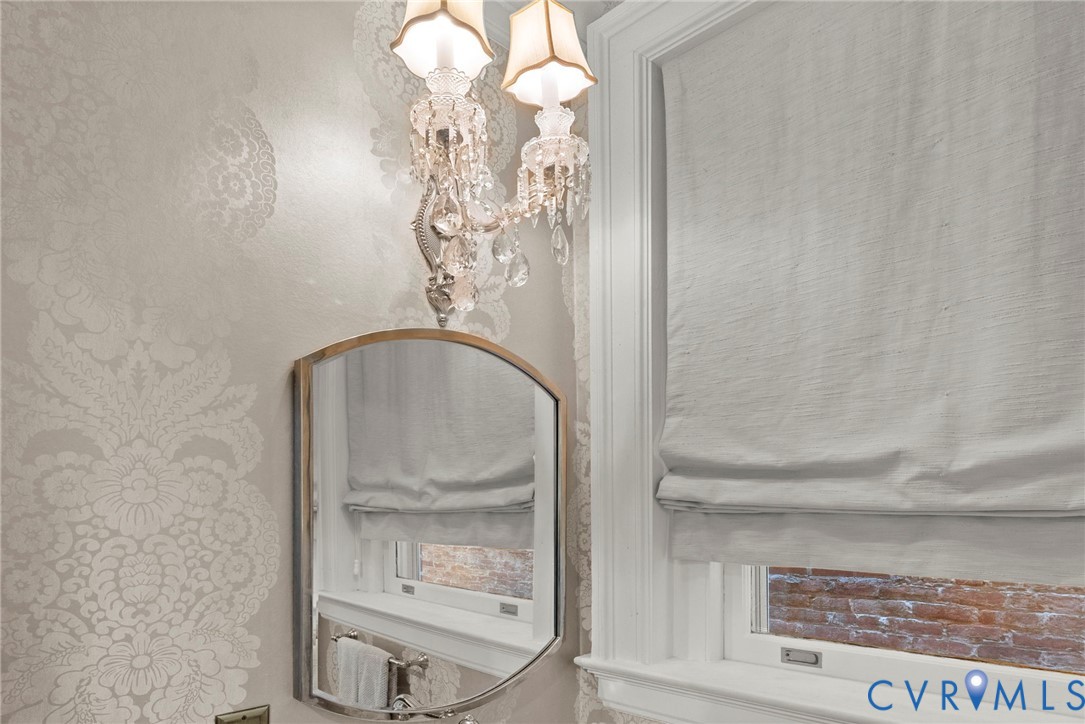 Crystal-accented double wall sconce, ornate damask-patterned wallcovering, arched metal-framed mirror, and custom window casing with integrated sill