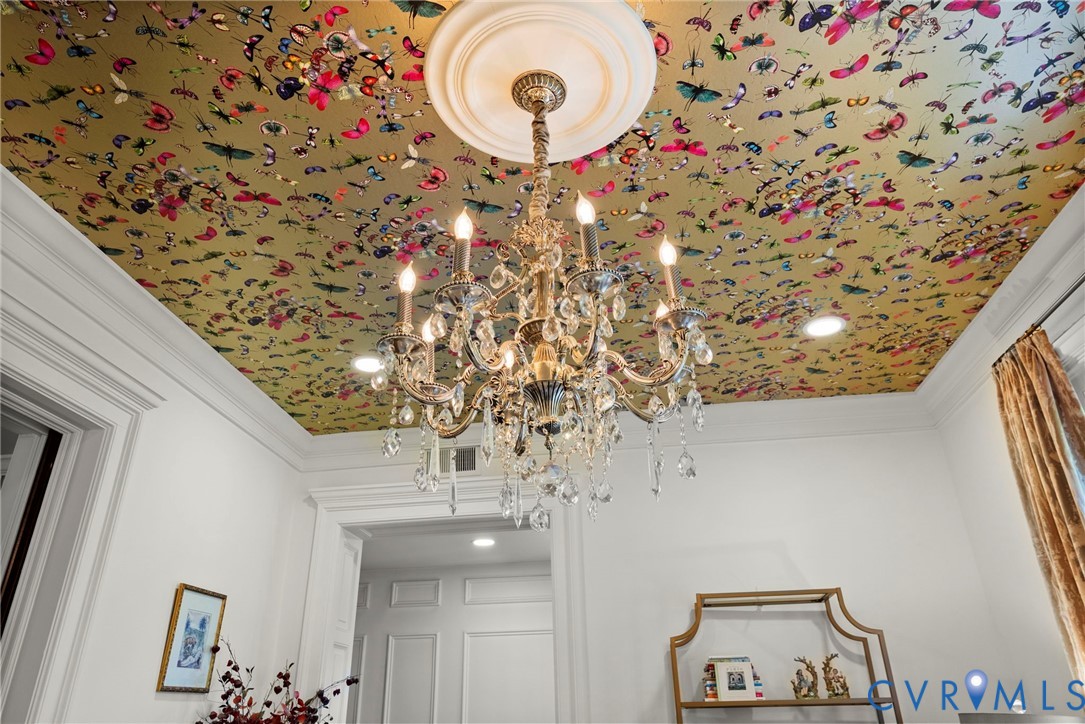 Intricate multi-arm crystal chandelier suspended from a ceiling medallion, set against a gold-tone ceiling featuring a decorative insect and butterfly motif, complemented by crown molding