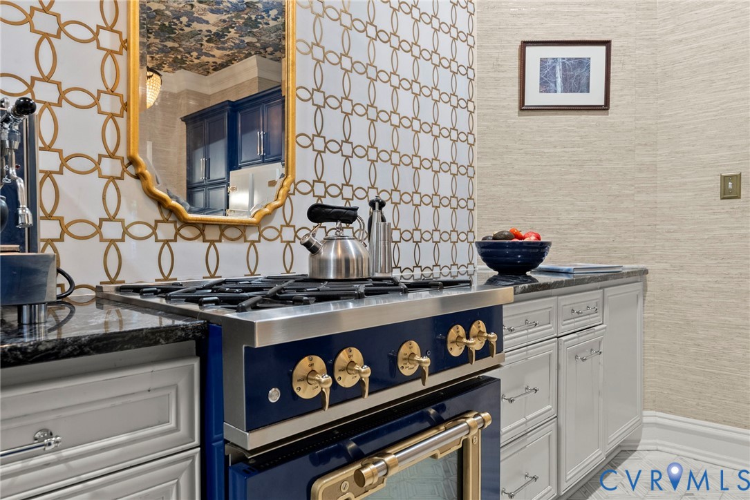 Custom blue-finish professional-grade gas range, geometric-patterned backsplash tile, neutral textured wall covering, and polished stone-finish countertops with inset cabinetry