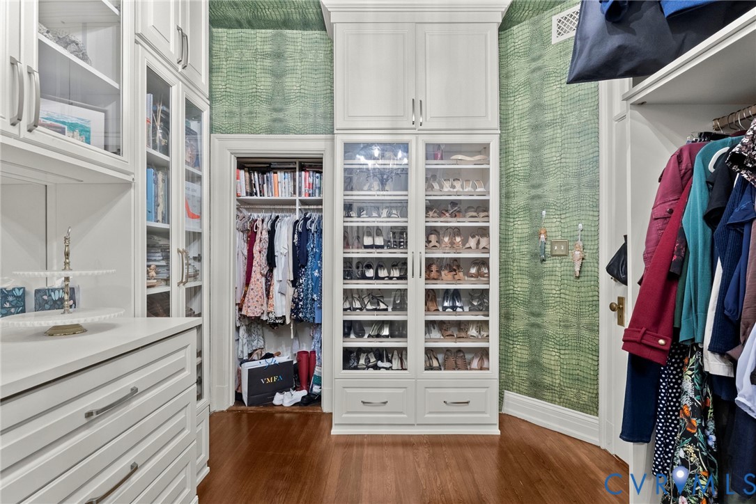 Custom-built cabinetry featuring floor-to-ceiling glass-front doors, integrated upper storage units, extensive built-in shelving, and hardwood flooring