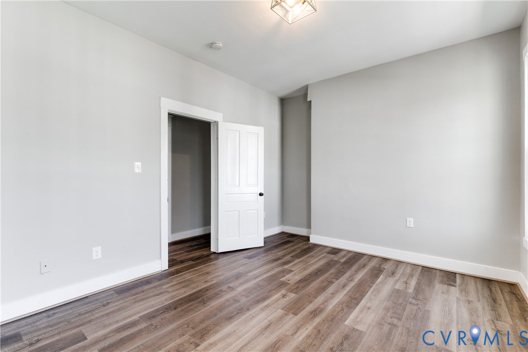 Room featuring wood-finish flooring, neutral walls, a white four-panel door, and a geometric flush-mount light fixture