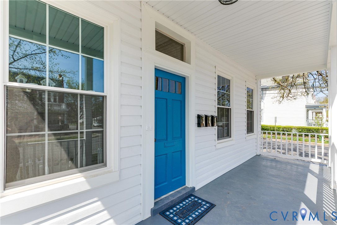 Covered front porch featuring white horizontal siding, a solid entry door with transom window, and multi-pane windows with grid detailing