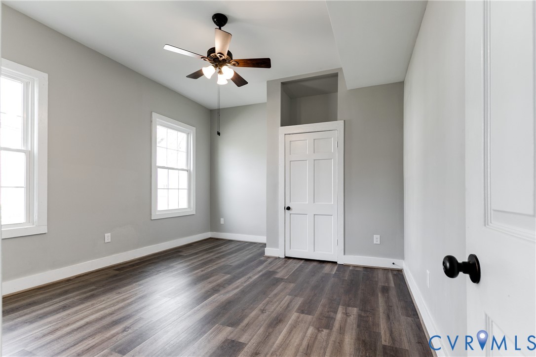 Room featuring wood-finish flooring, neutral wall paint, multi-pane windows, a six-panel door with matte black hardware, and an overhead ceiling fan with integrated lighting