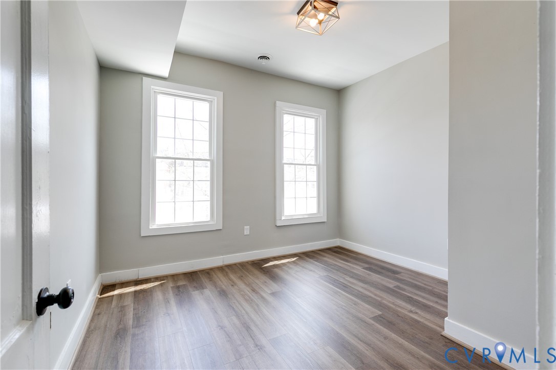 Neutral interior room featuring wood-finish flooring, two grid-pattern windows, and a geometric metal flush-mount light fixture