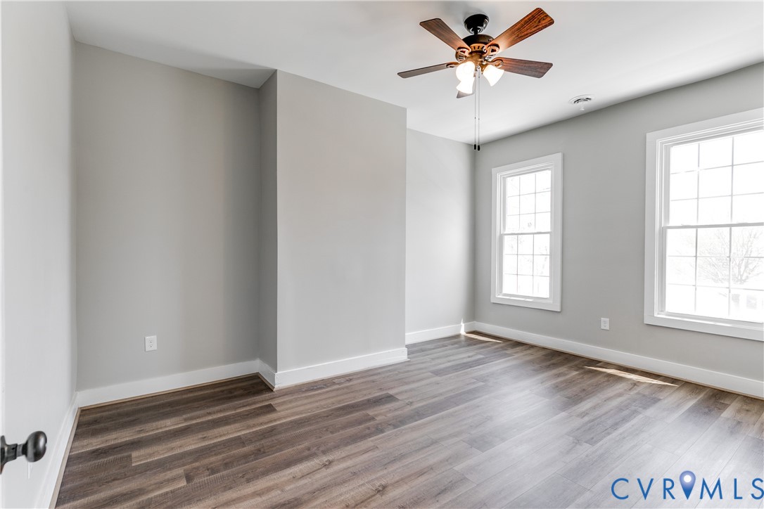 Neutral-toned room featuring wood-finish flooring, dual grid-pattern windows, and a ceiling fan with integrated lighting