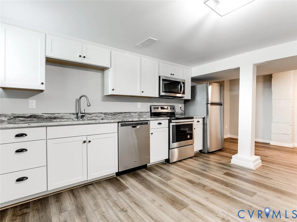 Kitchen featuring white cabinetry, stone-patterned countertops, stainless steel appliances, and wood-finish flooring