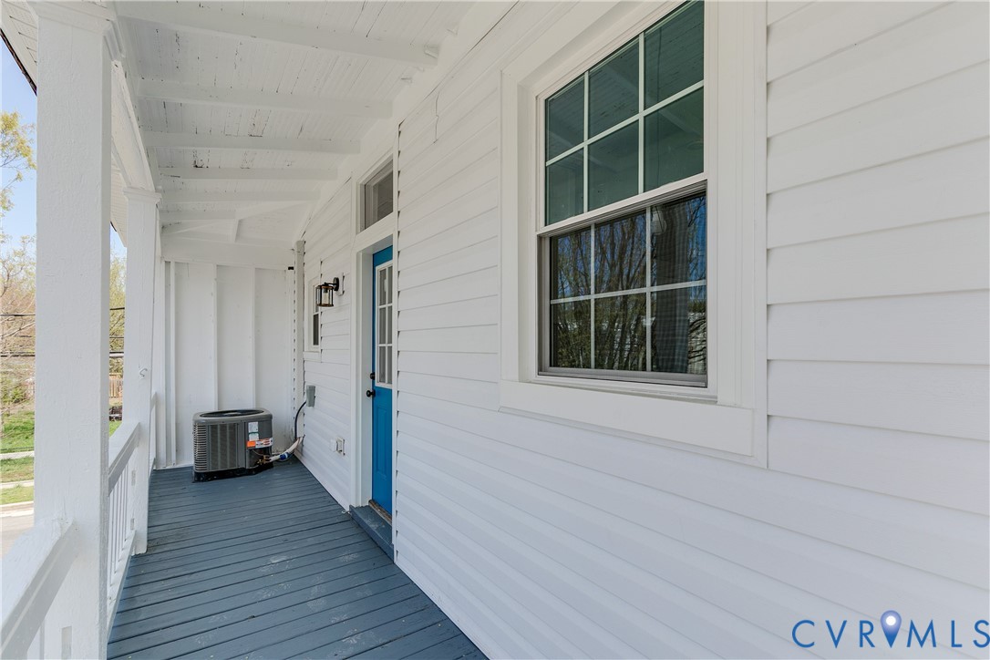 Covered porch featuring white horizontal siding, painted wood-plank flooring, a grid-pattern window, and a paneled entry door with a transom window