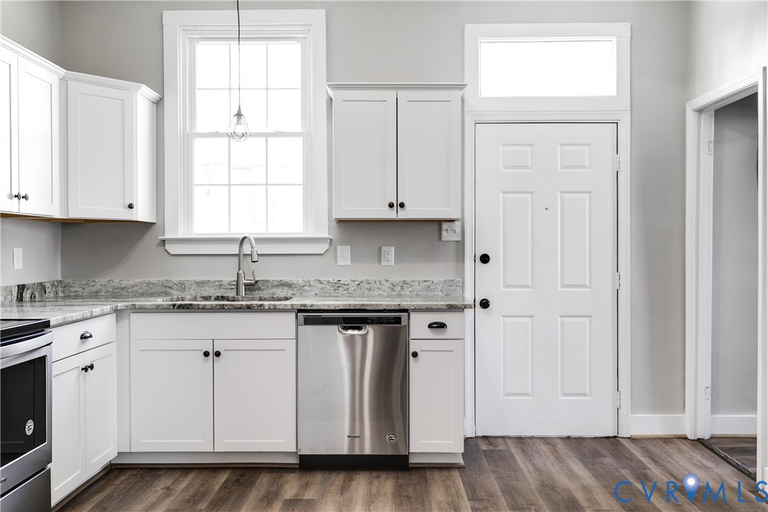 White shaker-style cabinetry, stone-patterned countertops, stainless steel dishwasher, wood-finish flooring, and a transom window above the entry door