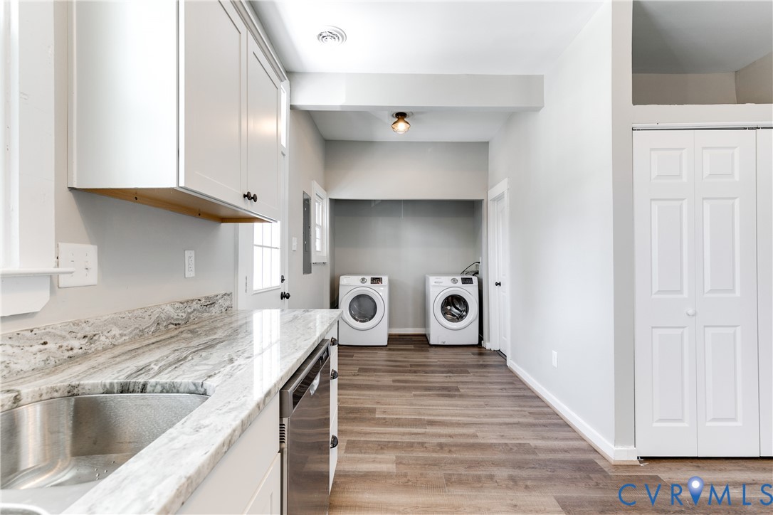 Laundry area featuring wood-finish flooring, white shaker-style cabinetry, natural stone-patterned countertops, a stainless steel undermount sink, and bi-fold closet doors