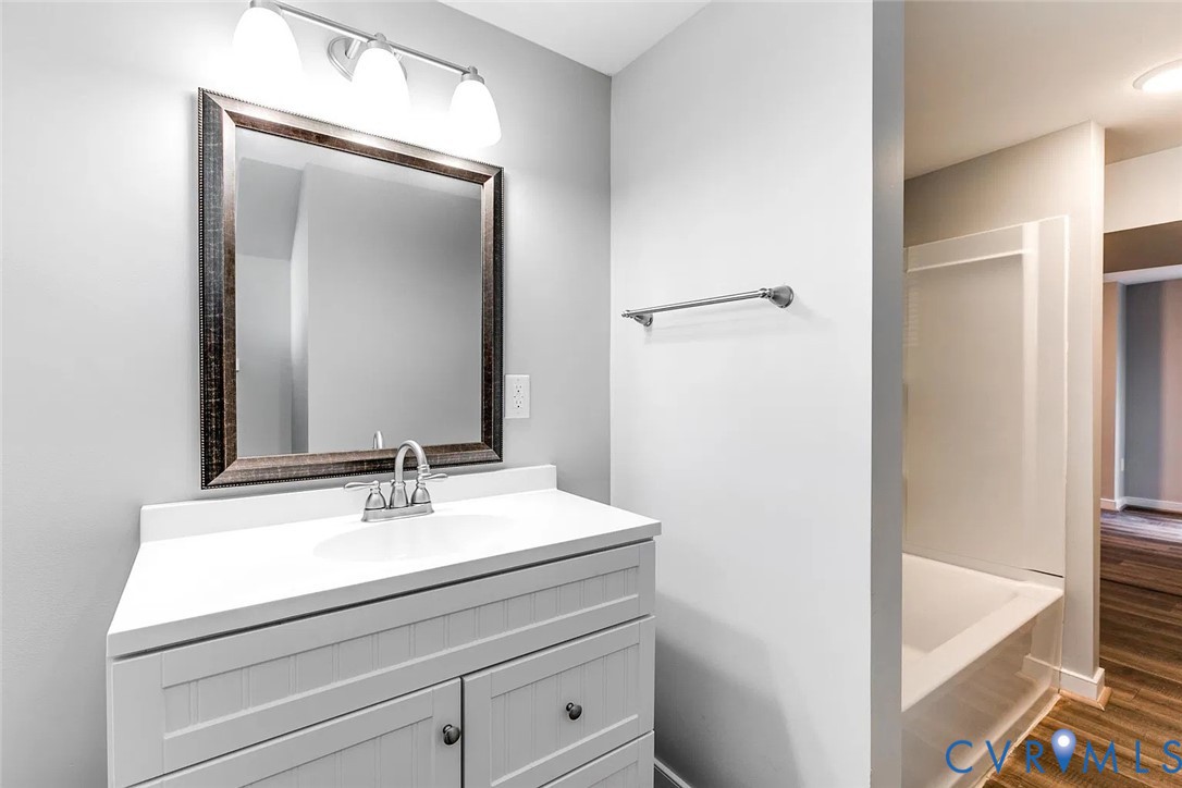 Bathroom vanity with a white countertop, integrated sink, shaker-style cabinetry, and a three-light vanity fixture