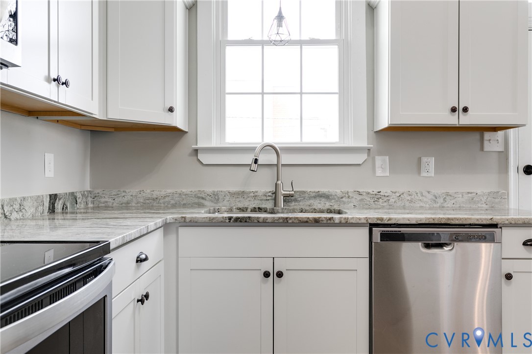 Kitchen featuring white shaker-style cabinetry, natural stone countertops, integrated stainless steel dishwasher, undermount sink with high-arc faucet, and a large multi-pane window