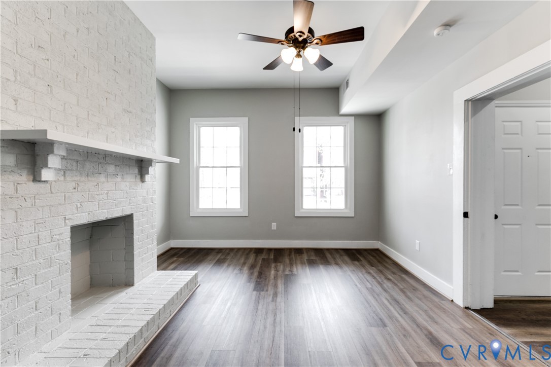 Painted brick fireplace with a mantle, wood-finish flooring, and a multi-light ceiling fan