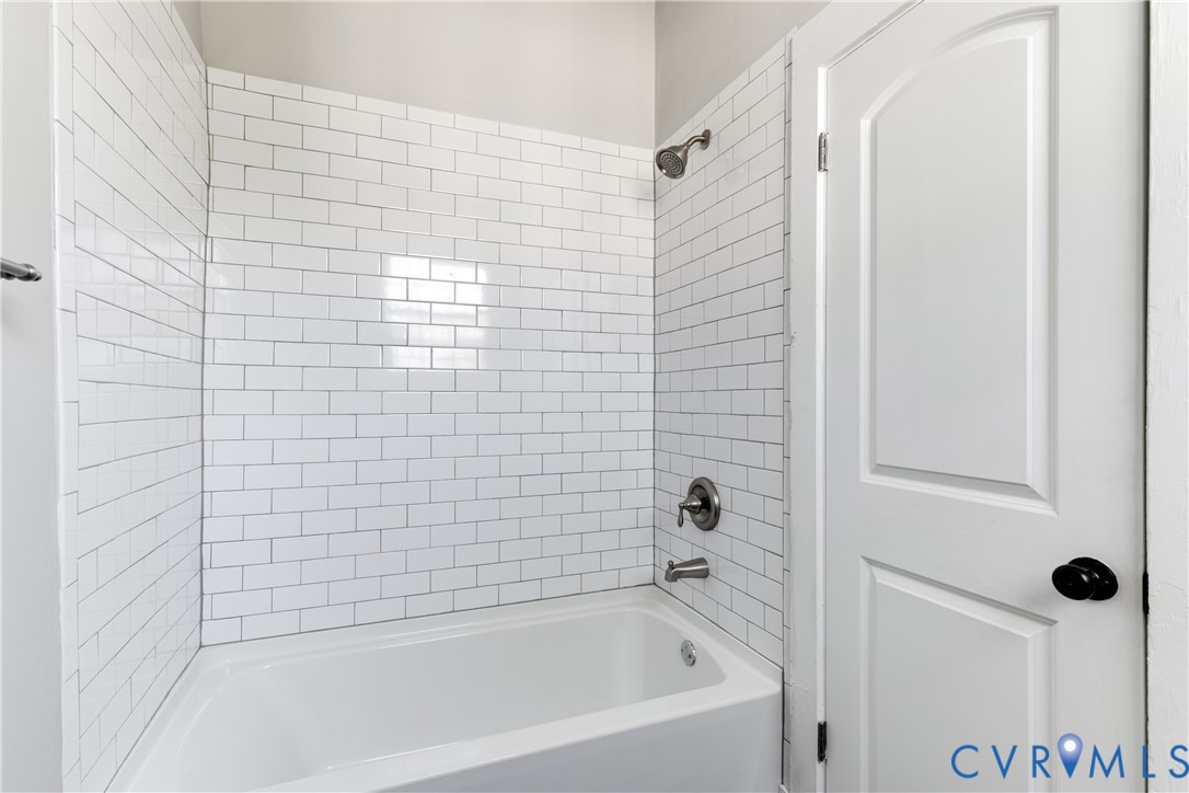 White subway tile surround, standard acrylic bathtub, brushed metal shower head and faucet hardware, and a white arched-panel door with a matte black handle