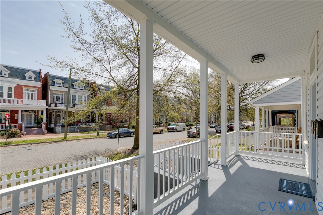 Covered front porch featuring a painted concrete floor, white spindle railings, square structural columns, and a beadboard ceiling