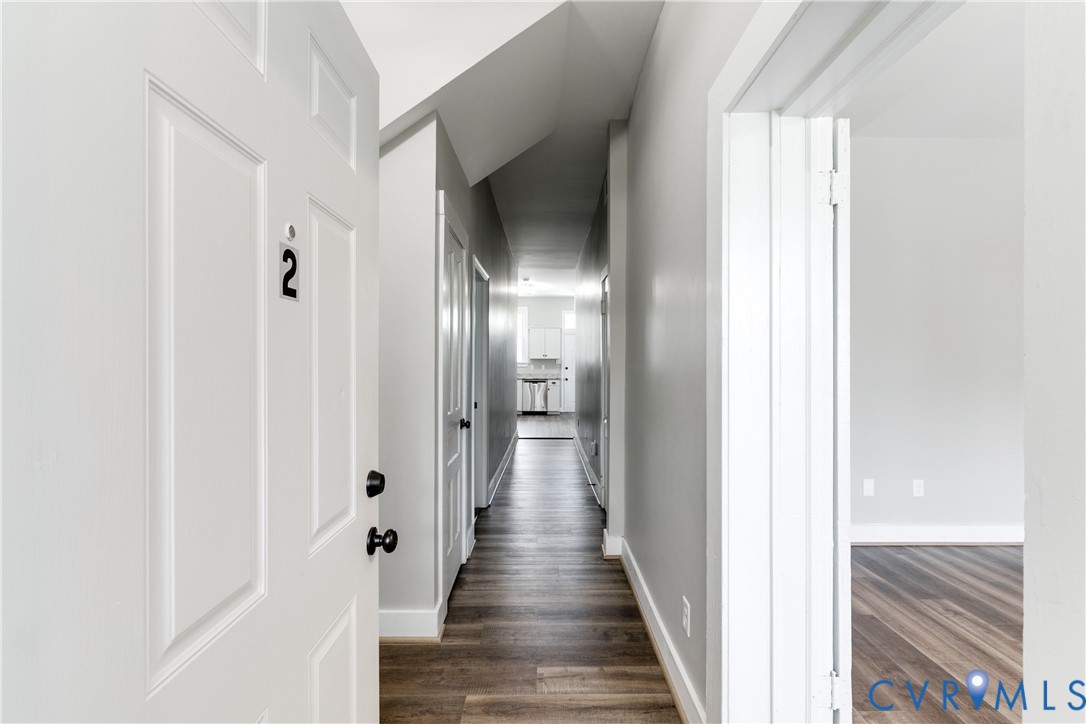 Interior hallway featuring wood-finish flooring, crisp neutral wall paint, and multiple interior doors with matte black hardware