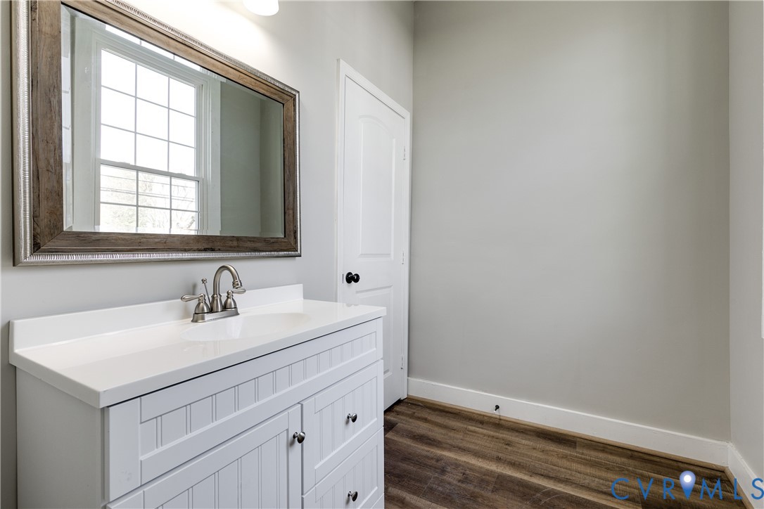 White beadboard vanity with a solid countertop, integrated basin, brushed metal faucet, and wood-finish flooring