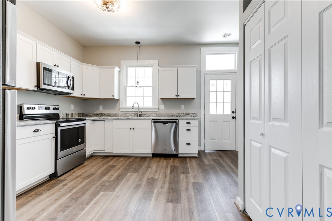 Kitchen featuring white cabinetry, stone-surface countertops, stainless steel appliances, wood-finish flooring, and a single-pane exterior door with a transom window