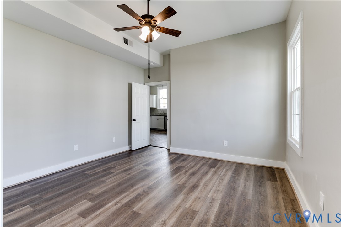 Room featuring wood-finish flooring, a tray ceiling, multi-blade ceiling fan with integrated lighting, and a multi-pane window