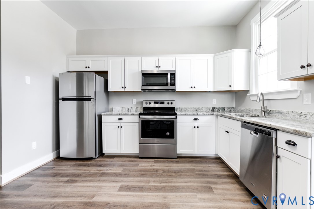 Kitchen featuring white shaker-style cabinetry, stone-surface countertops, stainless steel appliances, and wood-finish flooring