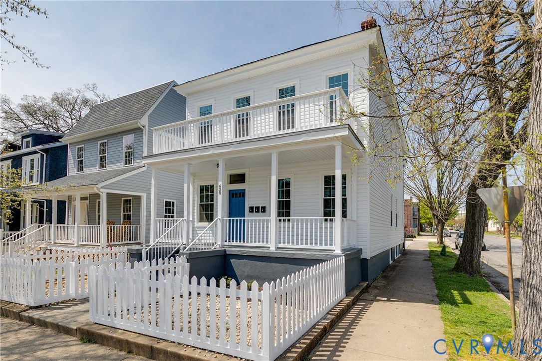 Two-story residence featuring horizontal lap siding, an expansive full-width front porch, a second-story balcony with white balustrades, and a white picket fence enclosing the front yard Two-story residence featuring horizontal lap siding, an expansive full-width front porch, a second-story balcony with white balustrades, and a white picket fence enclosing the front yard