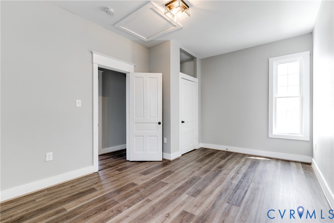Room featuring wood-finish flooring, crisp white trim, a single-hung window, solid-core panel doors, and a glass-paneled ceiling light fixture