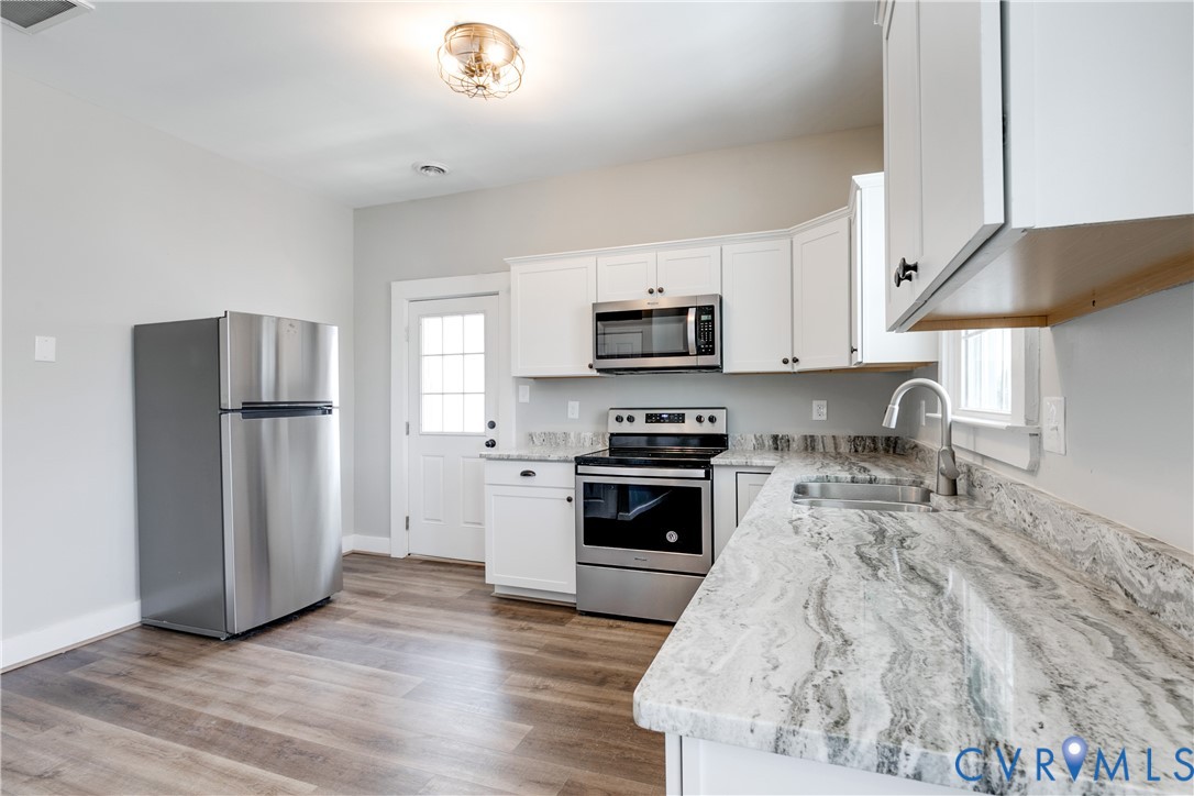 Kitchen featuring white cabinetry, stone-patterned countertops, stainless steel appliances, and wood-finish flooring