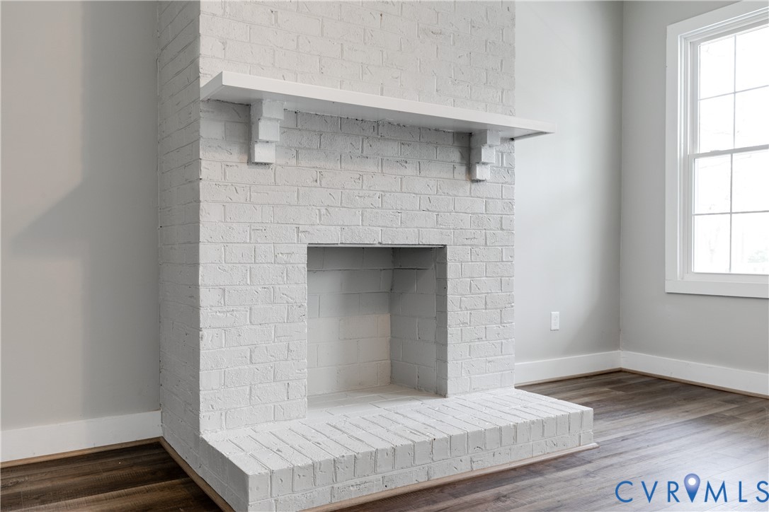 Floor-to-ceiling painted brick fireplace featuring a wood mantel, a raised brick hearth, and wood-finish flooring