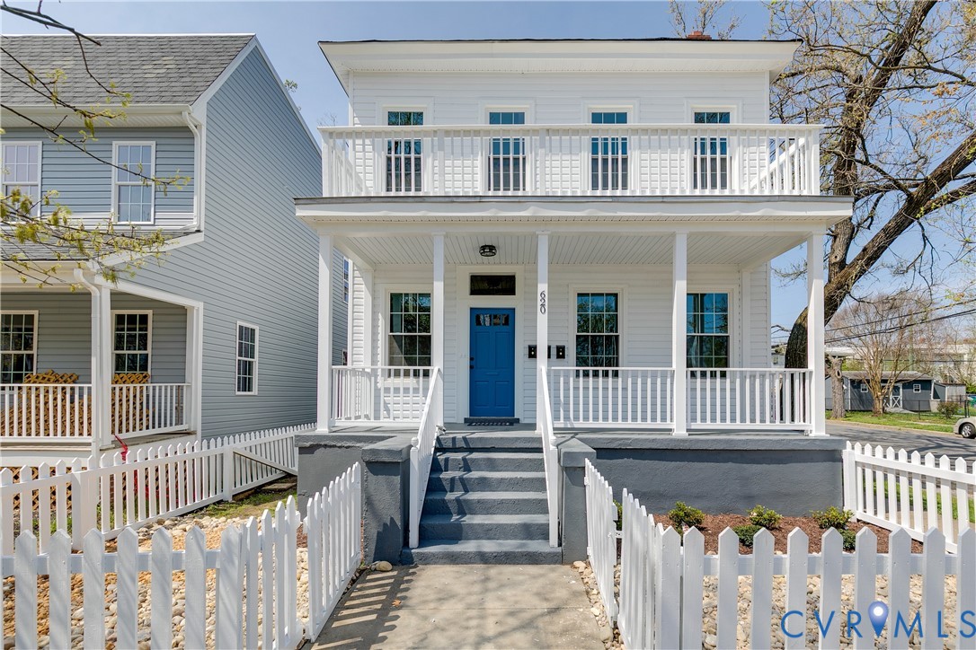 Two-story exterior featuring white horizontal siding, a covered full-width front porch, an upper-level balcony with railings, and a solid blue entry door