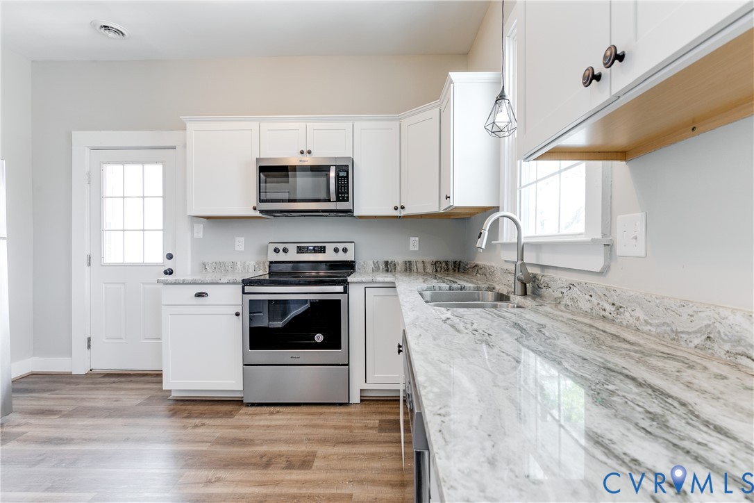 Kitchen featuring white shaker-style cabinetry, stone countertops, stainless steel appliances, wood-finish flooring, and a single-handle pull-down faucet