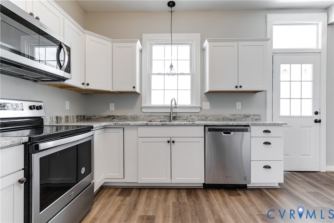 Kitchen featuring white cabinetry, stone-finish countertops, stainless steel appliances, wood-finish flooring, and a single-light pendant fixture