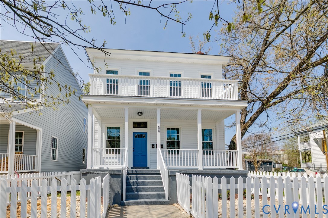 Two-story exterior featuring white horizontal siding, a covered front porch with a second-story balcony, and a white picket fence