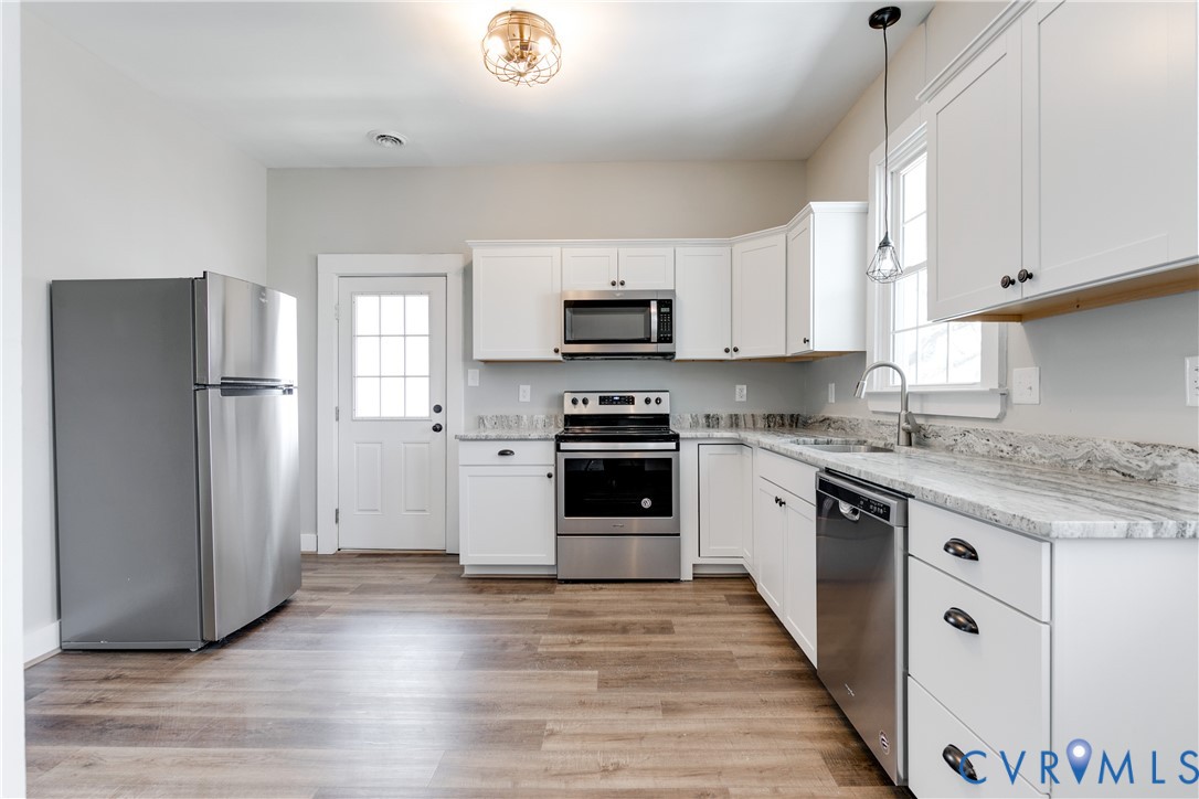 Kitchen featuring white shaker-style cabinetry, stone-finish countertops, stainless steel appliances, and wood-finish flooring