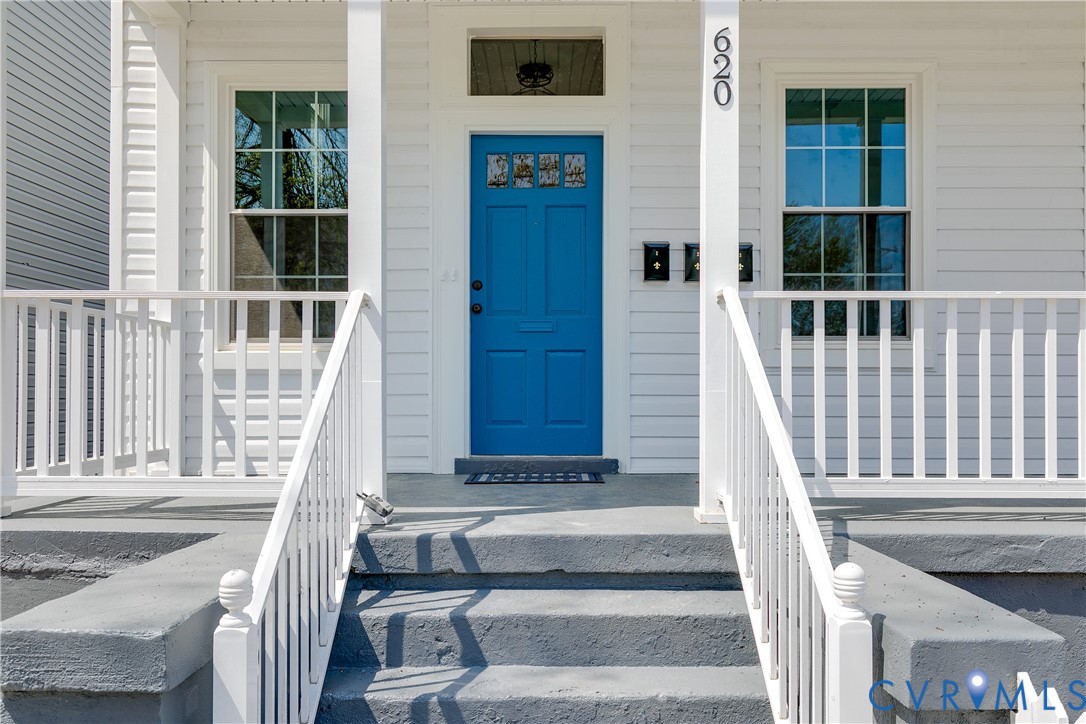 Covered front porch featuring white railings, gray concrete steps, lap siding, and a blue paneled front door with a transom window