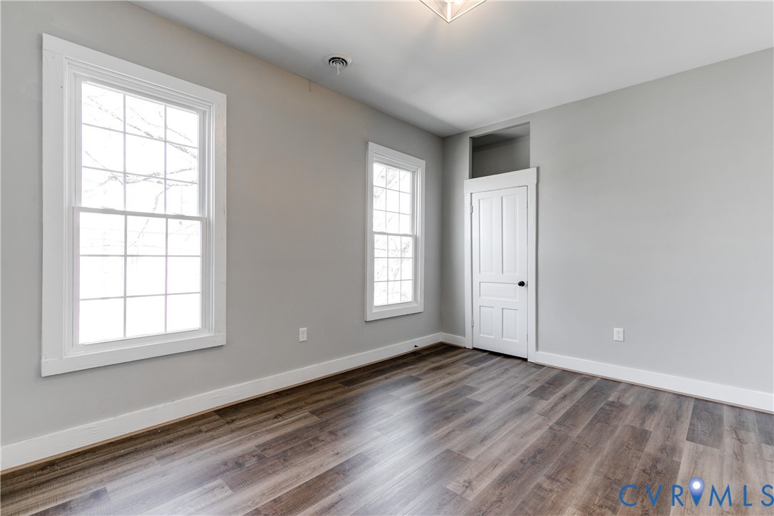 Interior room featuring wood-finish flooring, two multi-pane windows, and a single-panel door with an integrated transom