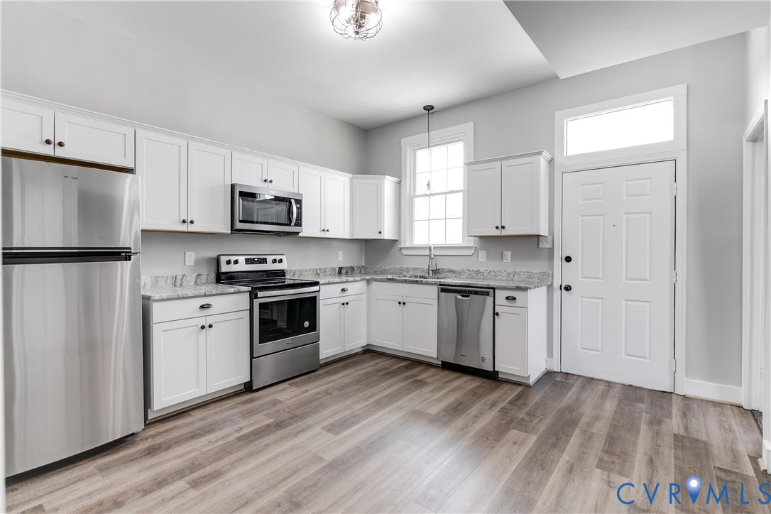 Kitchen featuring shaker-style white cabinetry, stone-finish countertops, stainless steel appliances, wood-finish flooring, and a transom window above the door