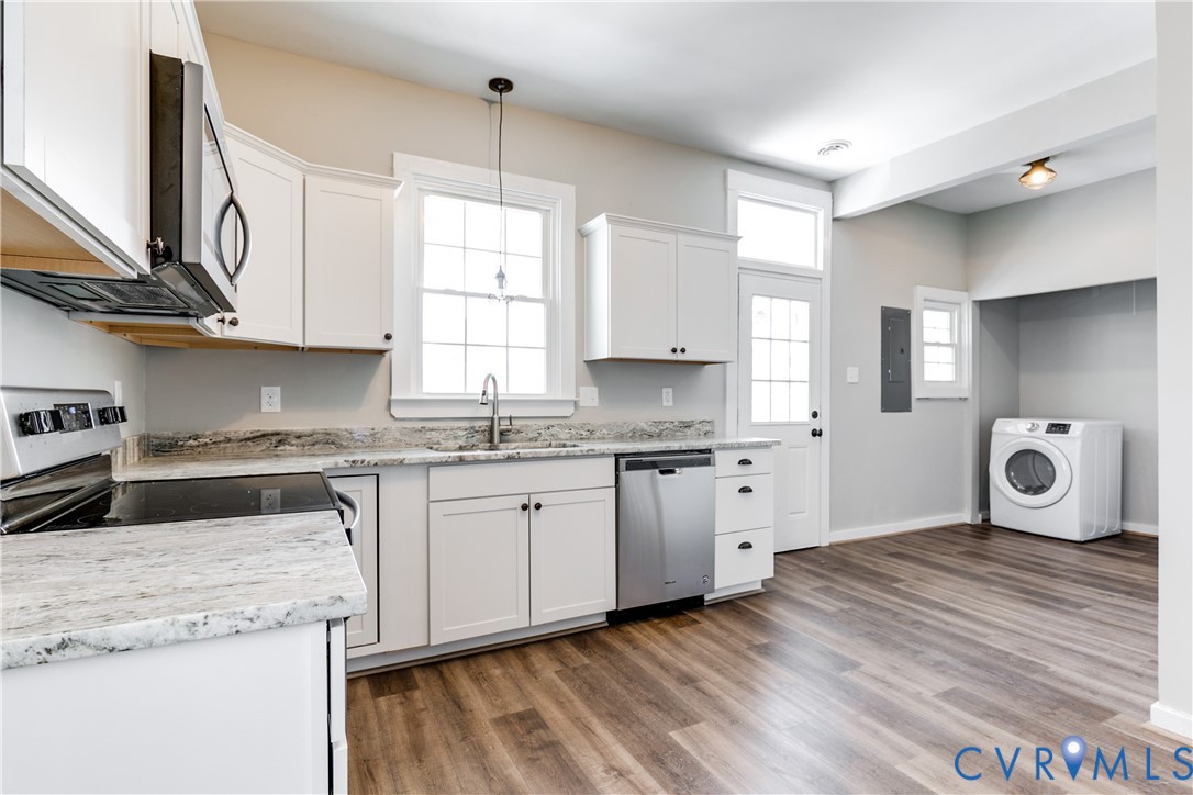 Kitchen featuring white cabinetry, light-toned stone-finish countertops, stainless steel appliances, wood-finish flooring, and a dedicated laundry area