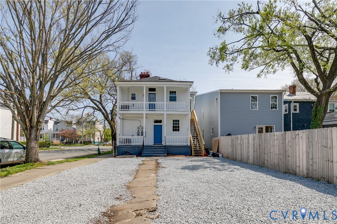 Two-story exterior featuring a stacked double-tiered porch, white balustrades, concrete walkway, and gravel-surfaced lot