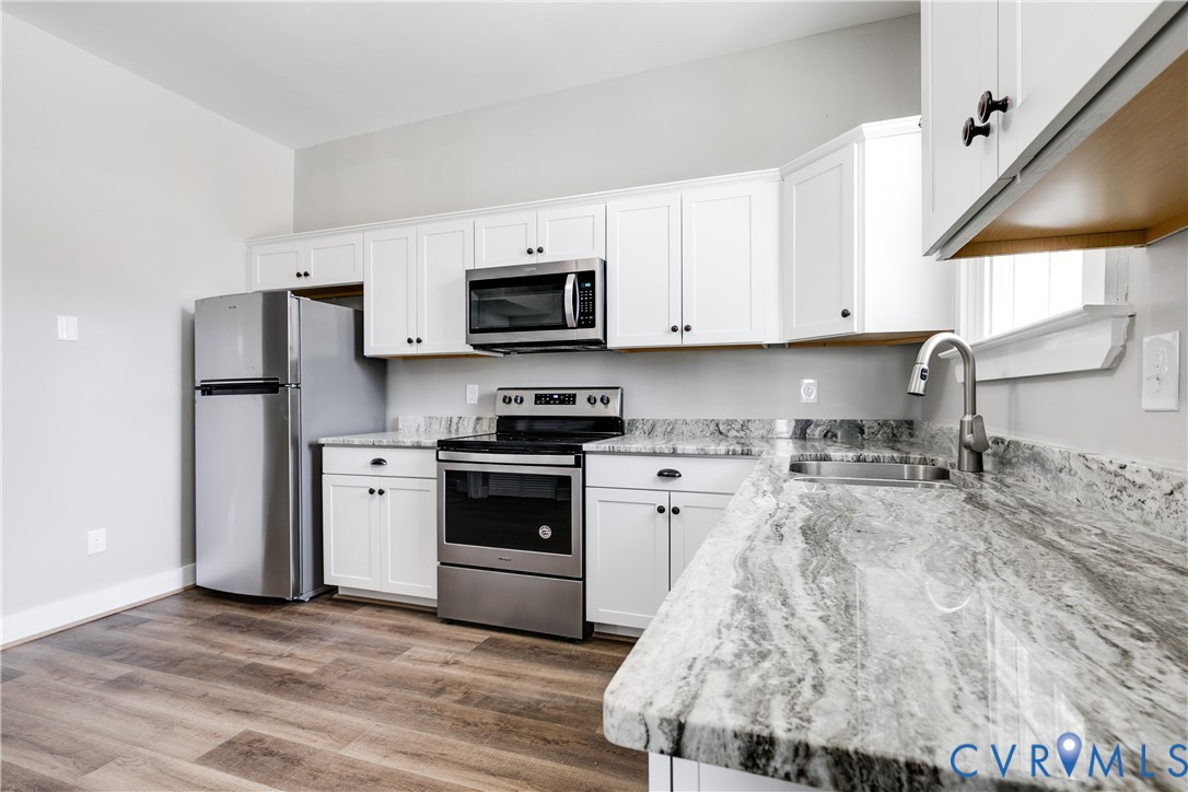 Kitchen featuring white shaker-style cabinetry, high-contrast stone countertops, stainless steel appliances, and wood-finish flooring