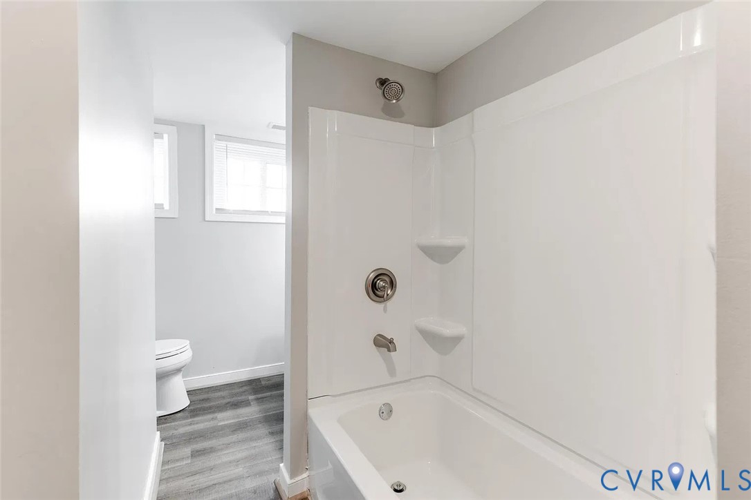 Bathroom featuring a tub-shower combination with integrated shelving, metallic finish hardware, wood-finish flooring, and white cabinetry