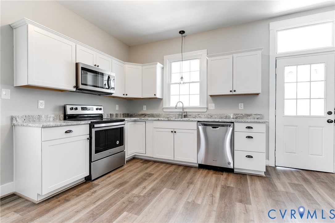Kitchen featuring white cabinetry, stone-surface countertops, stainless steel appliances, wood-finish flooring, and a single-light exterior door with a transom window