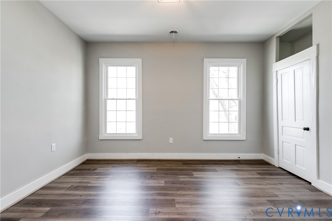 Room featuring wood-finish flooring, two multi-pane windows with white trim, neutral wall paint, and a classic four-panel door with a transom window